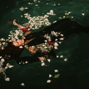 Woman in a black dress floating in water, surrounded by red and white flowers