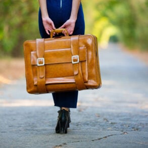 Woman holding suitcase on empty, bright road