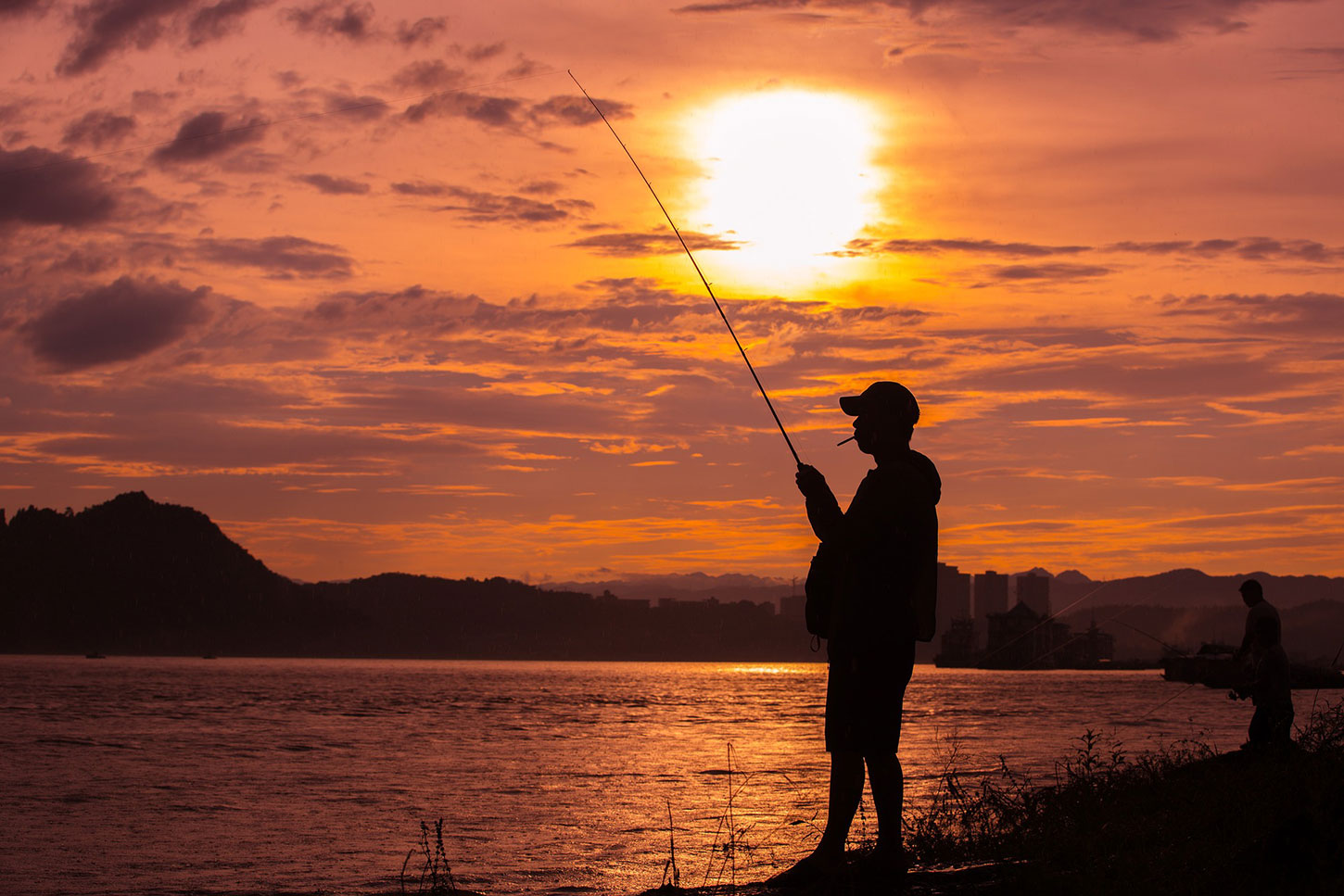 Silhouette of fisherman on lakeshore at sunset