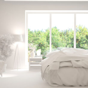 White bedroom with green trees outside windows