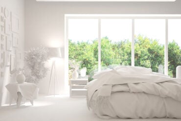 White bedroom with green trees outside windows