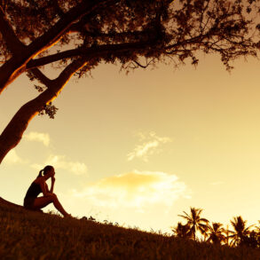Silhouette of woman sitting by tree at sunset