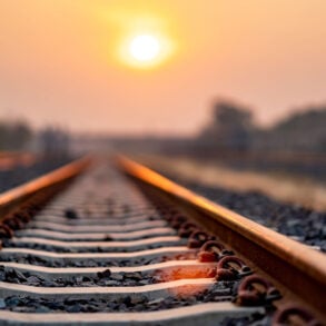 Train tracks under an orange sky with sun