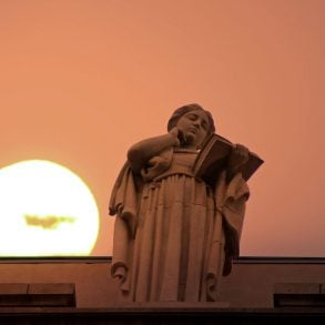 Statue of woman reading, with sun in background