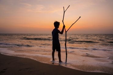 Silhouette of boy with stick on beach of Indian Ocean