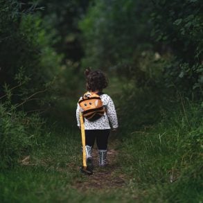 young girl with a backpack walking away through a forest