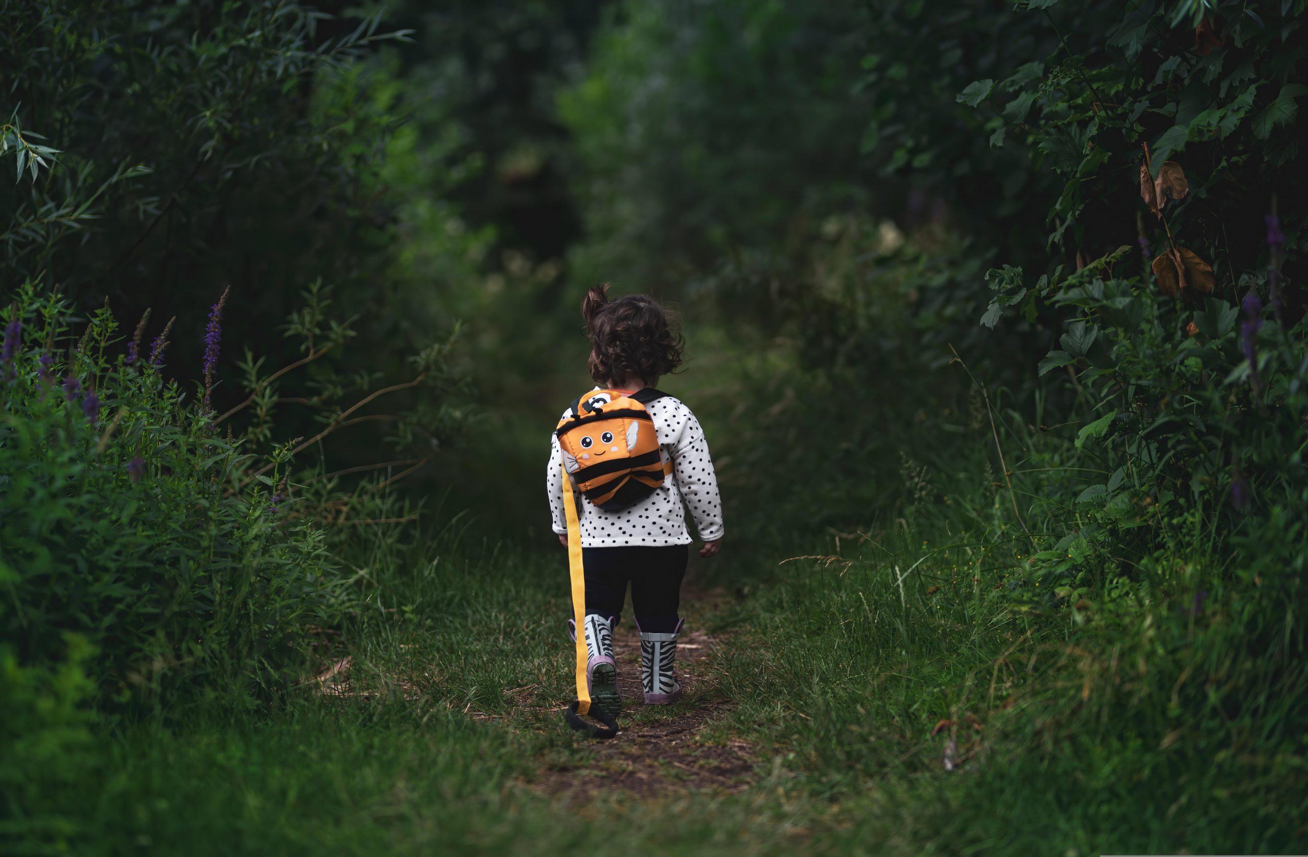 young girl with a backpack walking away through a forest