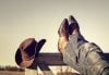 Boots and jeans resting on Western fence with hat