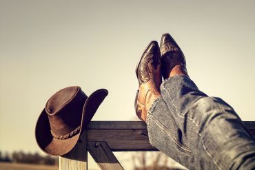 Boots and jeans resting on Western fence with hat