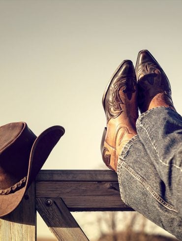 Boots and jeans resting on Western fence with hat