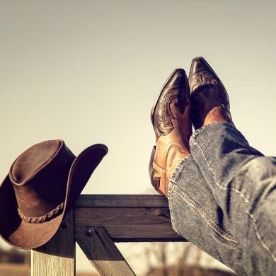Boots and jeans resting on Western fence with hat