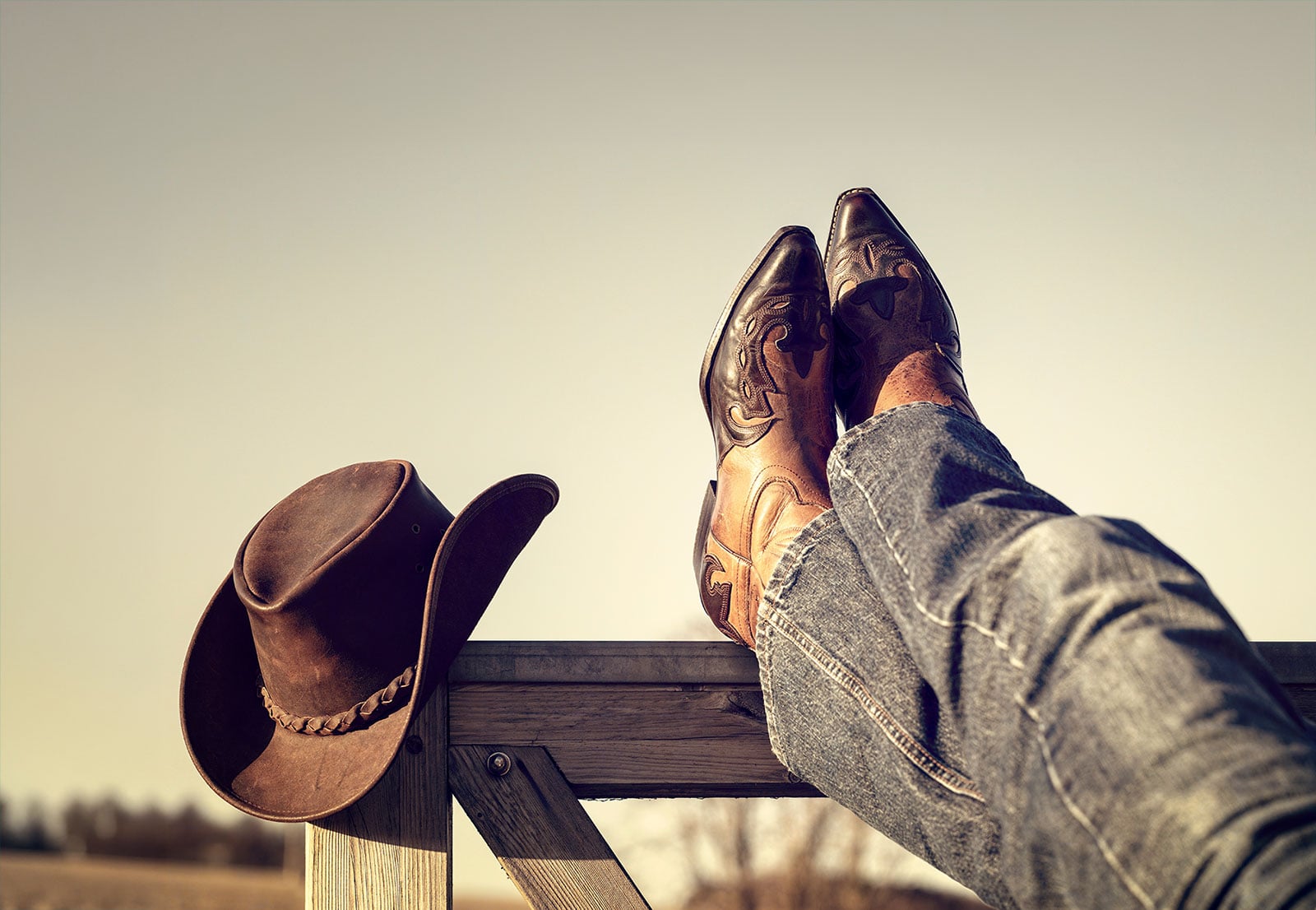 Boots and jeans resting on Western fence with hat